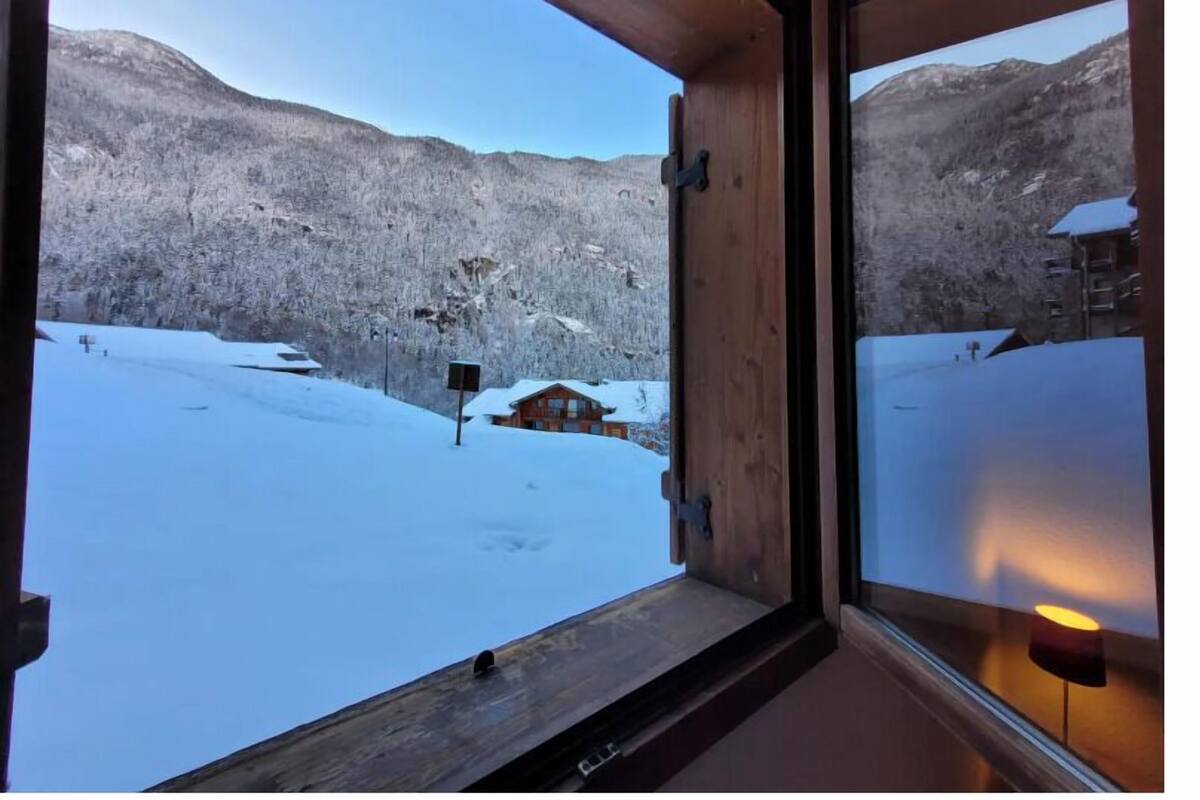 Una ventana con marco de madera que muestra un paisaje nevado y una cabaña.