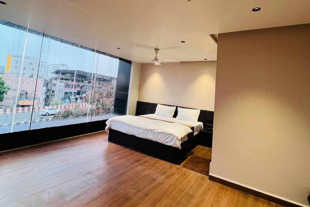 A modern bedroom with a large bed, a ceiling fan, and a view of the city through large windows.