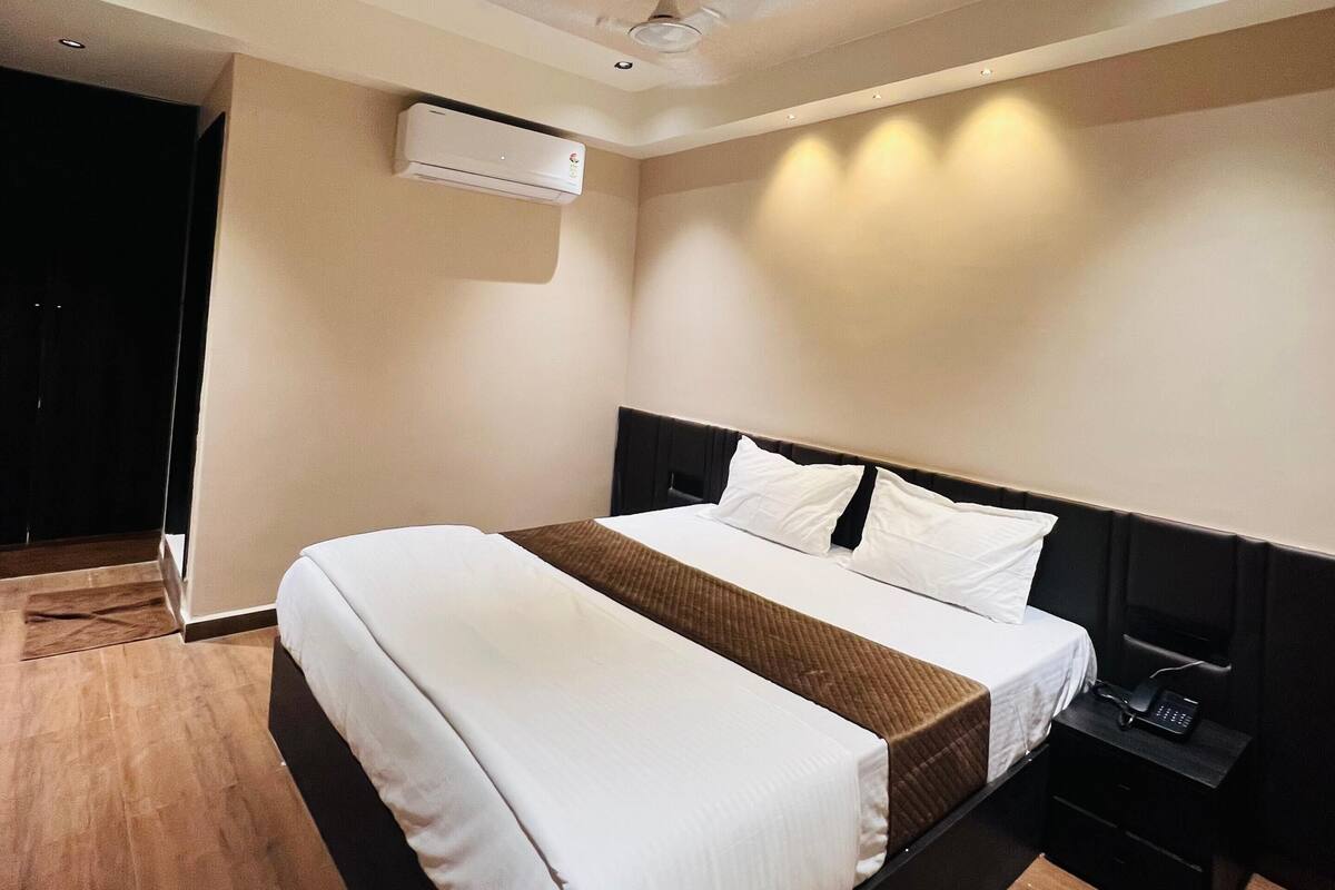 A modern hotel room with a large bed, a bedside table with a phone, an air conditioning unit, and a ceiling fan.