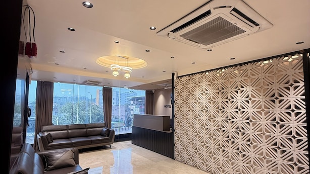 A modern hotel lobby with a reception desk, a sofa, a decorative partition, and a large window offering a city view. - Hotel Presidency (Surat)