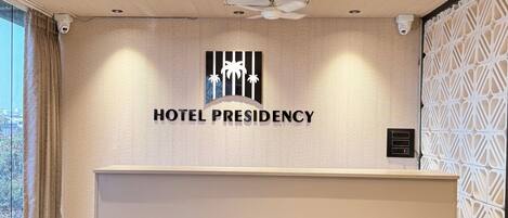 A hotel reception desk with a modern design, a ceiling fan, and a large window with curtains.