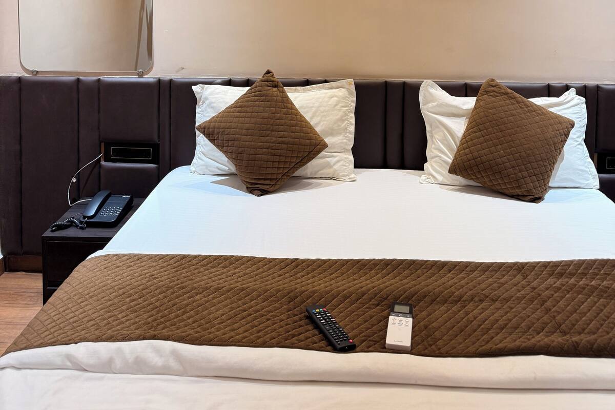 A hotel room with a bed, two pillows, a bedside table with a phone, and a wall-mounted mirror.