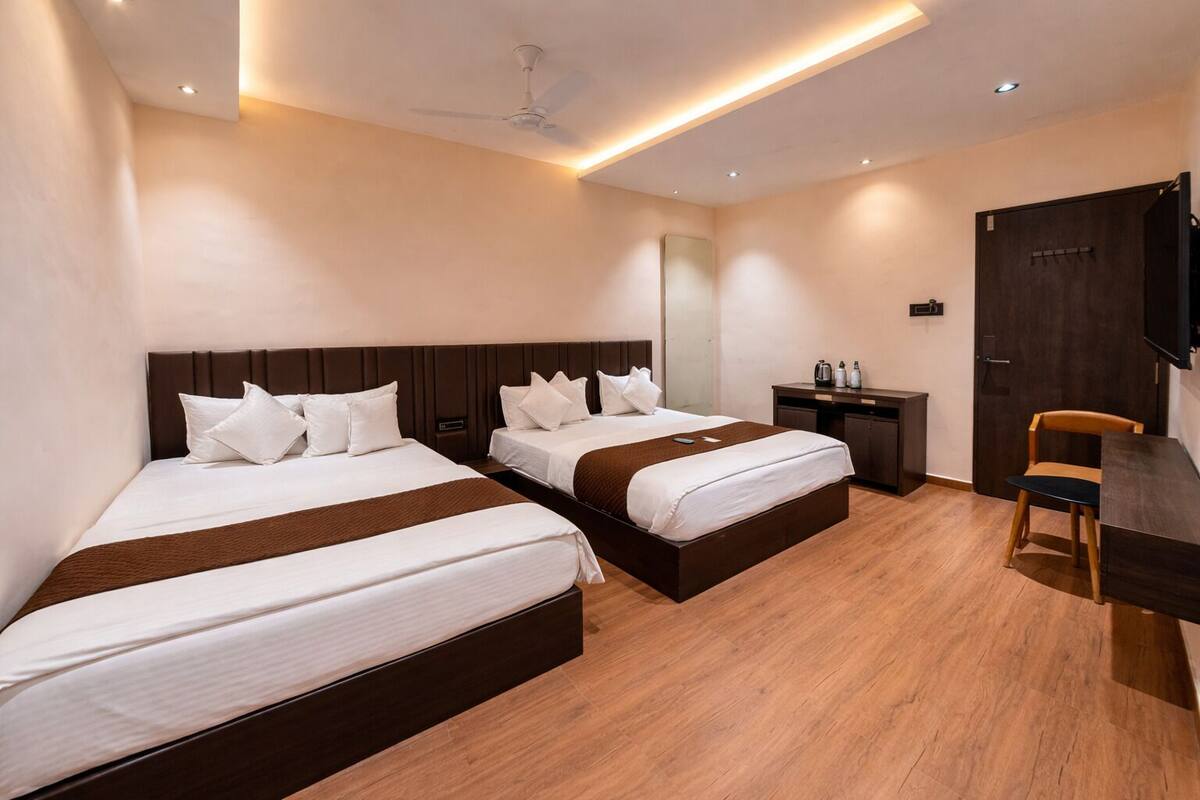 A hotel room with two beds, a desk, a chair, a television, and a ceiling fan.