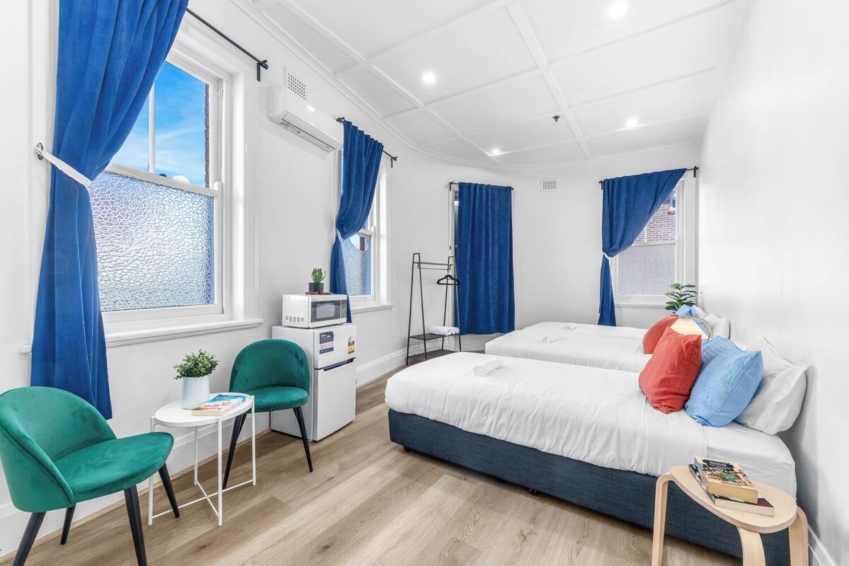 A modern hotel room with two beds, a desk, a chair, and a small table.