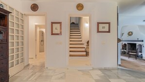 A spacious hallway with a marble floor, a wooden staircase, and a view of a fireplace area.
