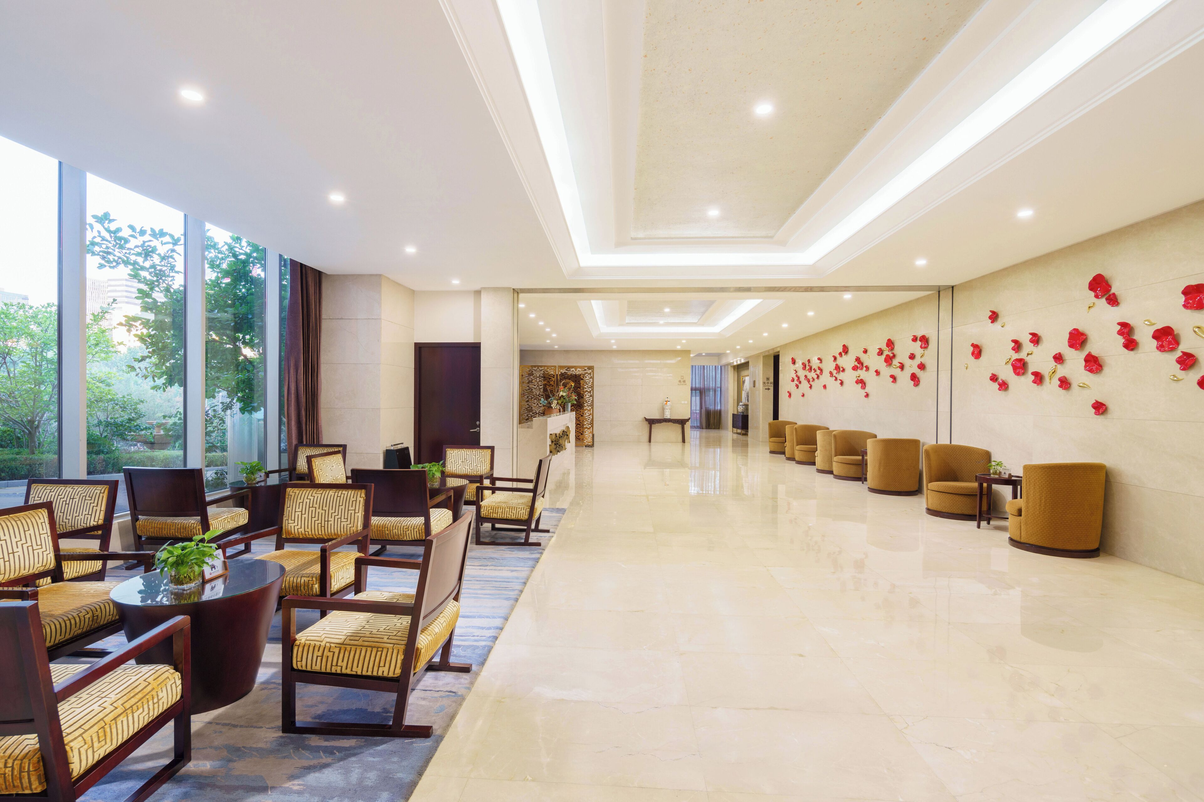 Un hall d’entrée spacieux avec un long comptoir de réception, plusieurs espaces aménagés avec des fauteuils et un mur décoré de fleurs rouges.