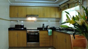 A kitchen with wooden cabinets, a stove, and a sink. - Westlands Gardens Apartment (Nairobi)