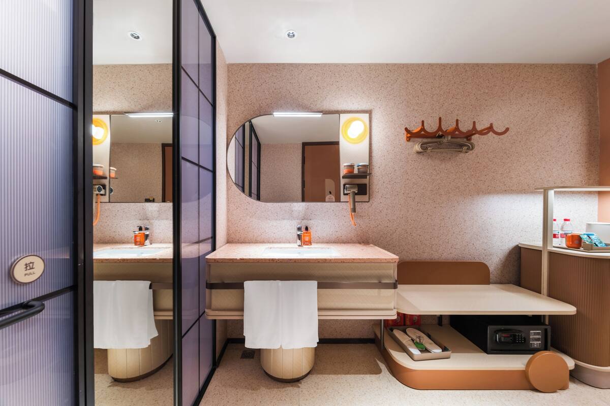 Un baño moderno con un espejo grande, dos lavamanos, un tocador y una mesita con un teléfono y un control remoto.