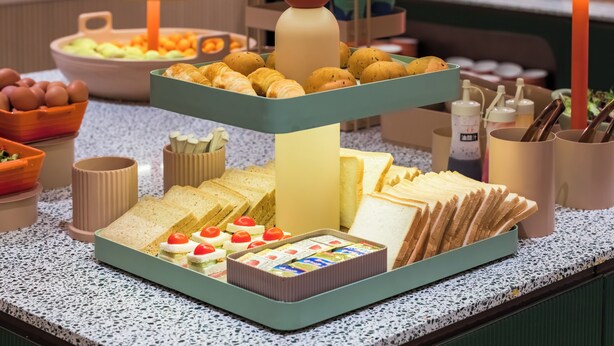 Un bufé con diversas opciones de comida, incluyendo pan, pastelería y una selección de quesos.