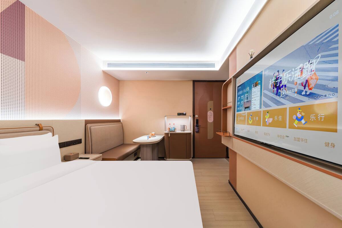 Habitación de hotel moderna con una cama grande, una mesita con una silla, un televisor montado en la pared y una ventana con persianas.