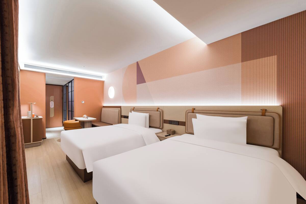Habitación de hotel con dos camas, una mesita, una mesita de noche y una pared con diseño geométrico.