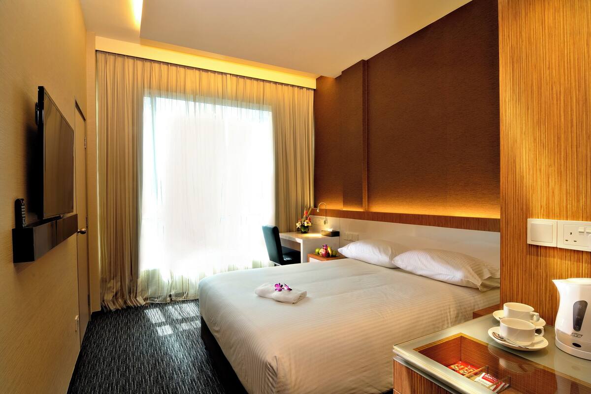 Une chambre d’hôtel équipée d’un lit, d’un bureau, d’une télévision, d’une machine à café et d’une fenêtre avec des rideaux.
