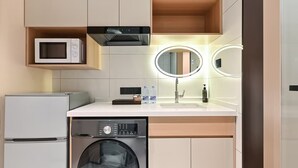 Eine kompakte Küche mit Mikrowelle, Backofen, Waschmaschine und Spüle mit Spiegel darüber.