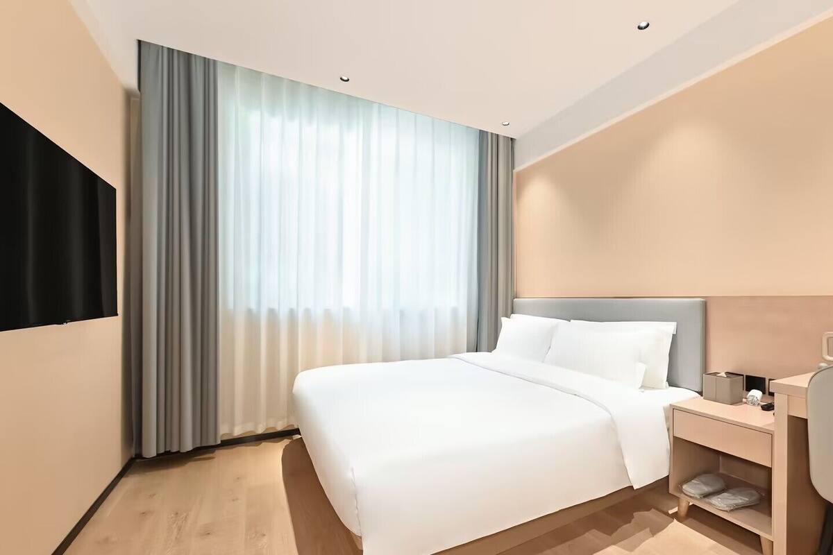 Ein modernes Hotelzimmer mit einem großen Bett, einem Nachttisch mit Lampe und einem an der Wand montierten Fernseher.