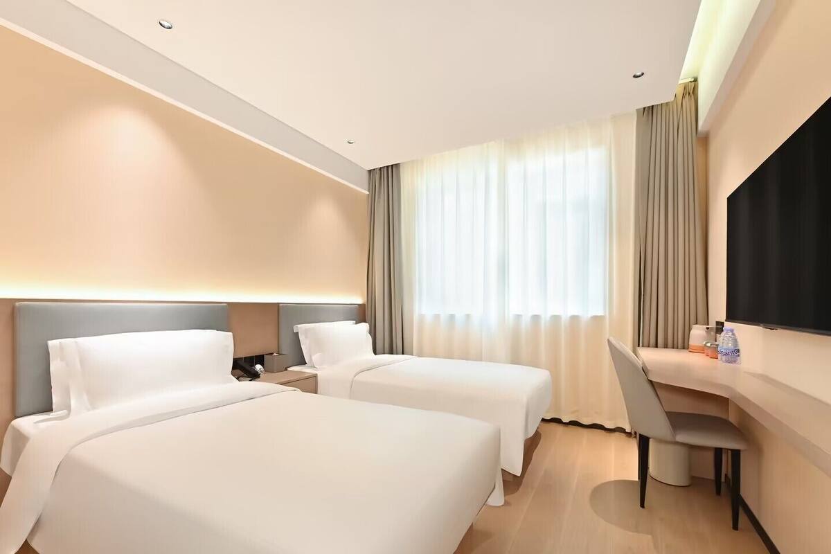 Ein Hotelzimmer mit zwei Betten, einem Schreibtisch, einem Sessel, einem Fernseher und einem Fenster mit Vorhängen.