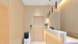 Ein moderner Empfangsbereich mit einer Rezeption, einem wandmontierten digitalen Bildschirm und einem Saugroboter.