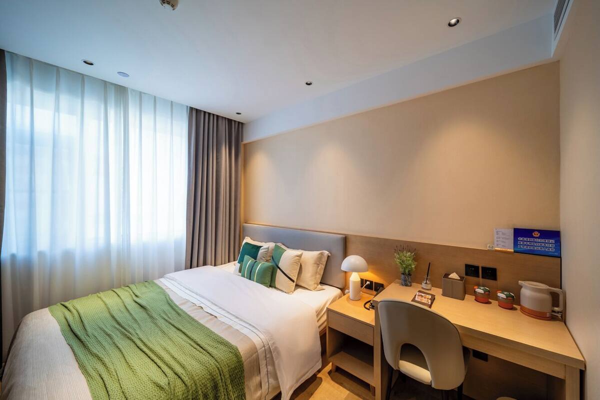 Ein Hotelzimmer mit Bett, Schreibtisch, Stuhl, Lampe, Kaffeemaschine und Pflanze.