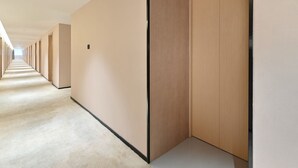 Ein langer, schmaler Gang mit Holztüren an einer Seite und beige gestrichenen Wänden.