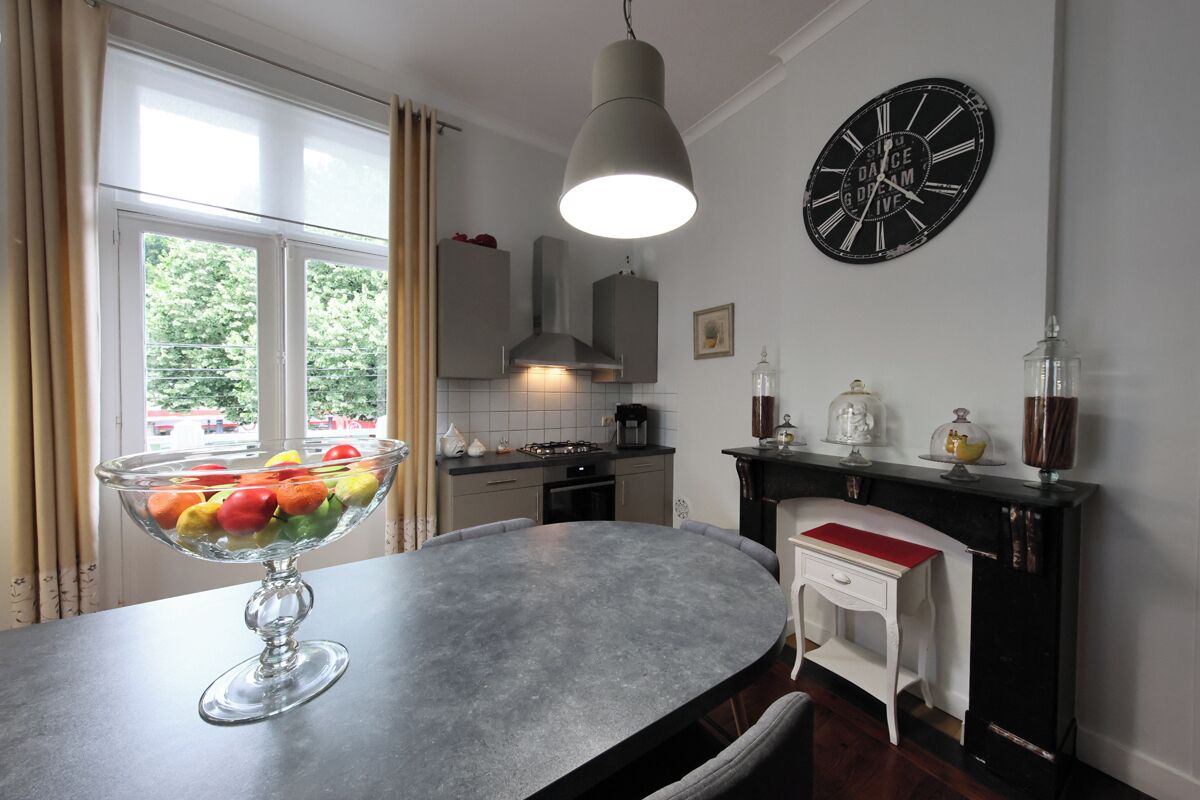 Een keuken met een ronde tafel, een schaal met fruit, een klok en een open haard.