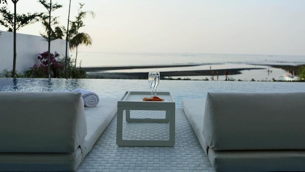 A poolside lounge with a table and two cushioned chairs, overlooking a beach and calm sea. - Lusa Beach Studios (Banjar)