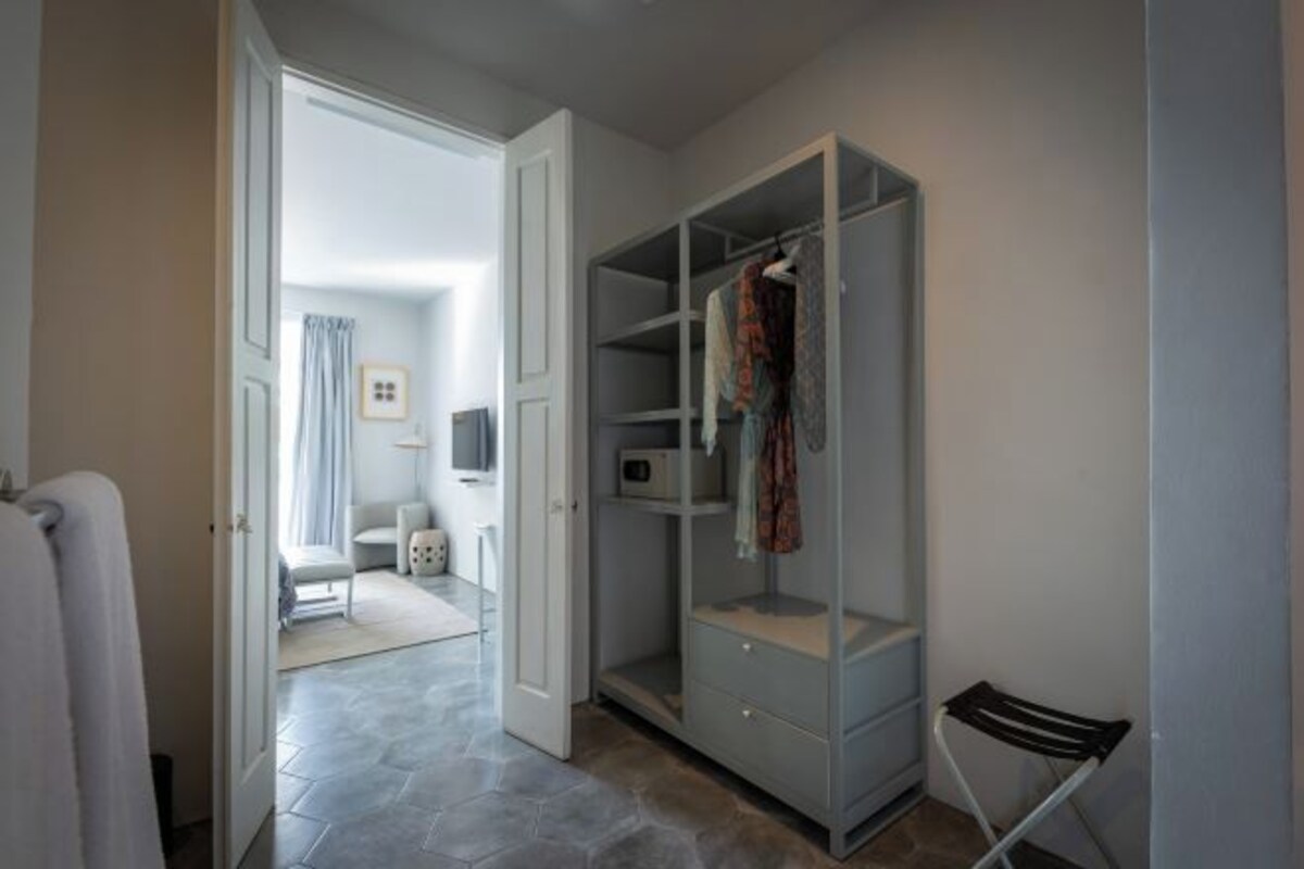 A walk-in closet with open doors, a chair, and a small table with a lamp.