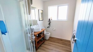 Ein Badezimmer mit einem Holzkosmetikschrank, einem weißen Waschbecken, einer Toilette und einer Dusche mit Glastür.