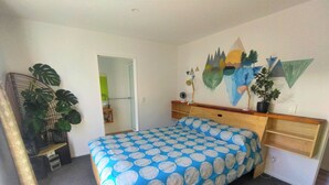Ein Schlafzimmer mit Bett, Nachttisch, Spiegel, Wandbild und einer Topfpflanze.