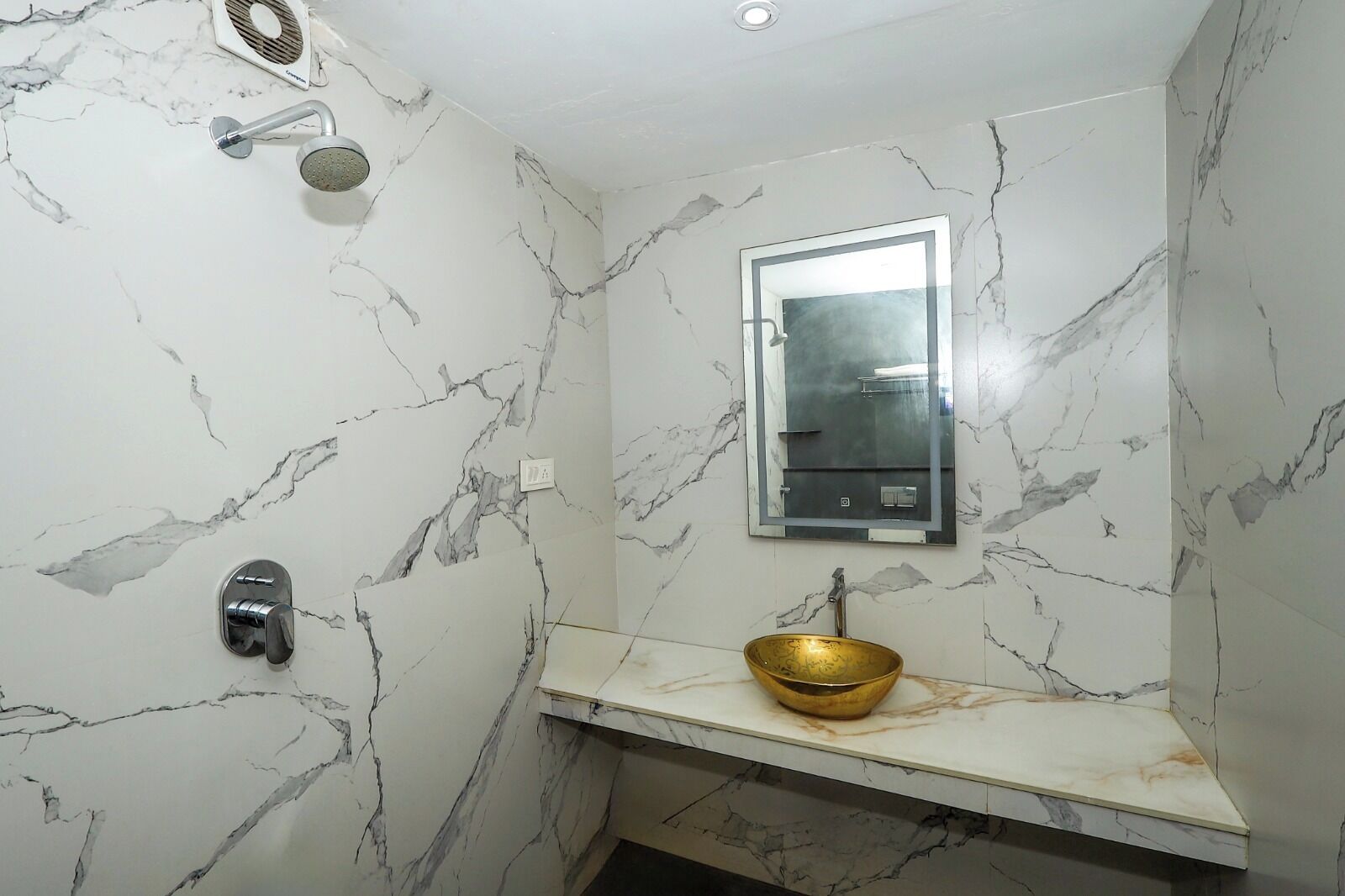 A bathroom with marble walls, a gold sink, a showerhead, and a mirror.