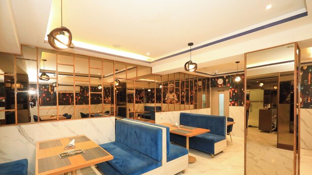Een modern restaurant met blauwe zitplaatsen, houten tafels en een spiegelwand.