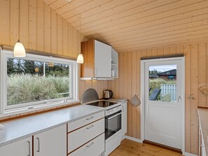 Cozinha compacta com paredes de madeira, forno embutido, fogão e janela com vista para o exterior.