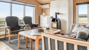 Interior acogedor de una cabaña con chimenea, muebles de madera y ventanas amplias con vistas.