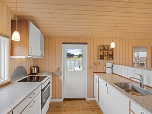 A modern kitchen with wooden walls, a built-in oven, a sink, and pendant lighting. - "Fridgerd" - 300m from the sea by Interhome (Løkken)