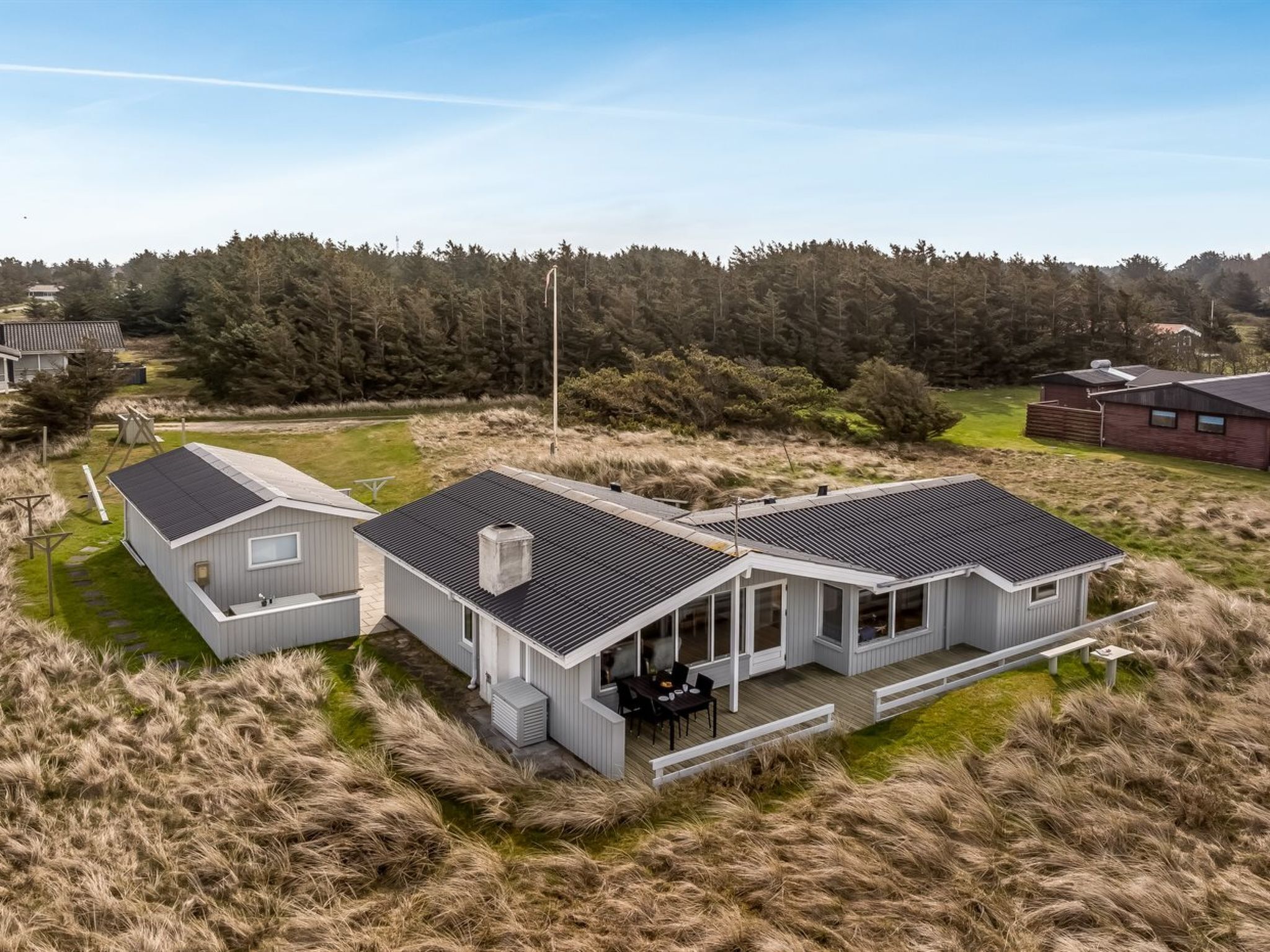 Une maison moderne dotée d’une grande terrasse, entourée d’un paysage naturel et d’arbres.