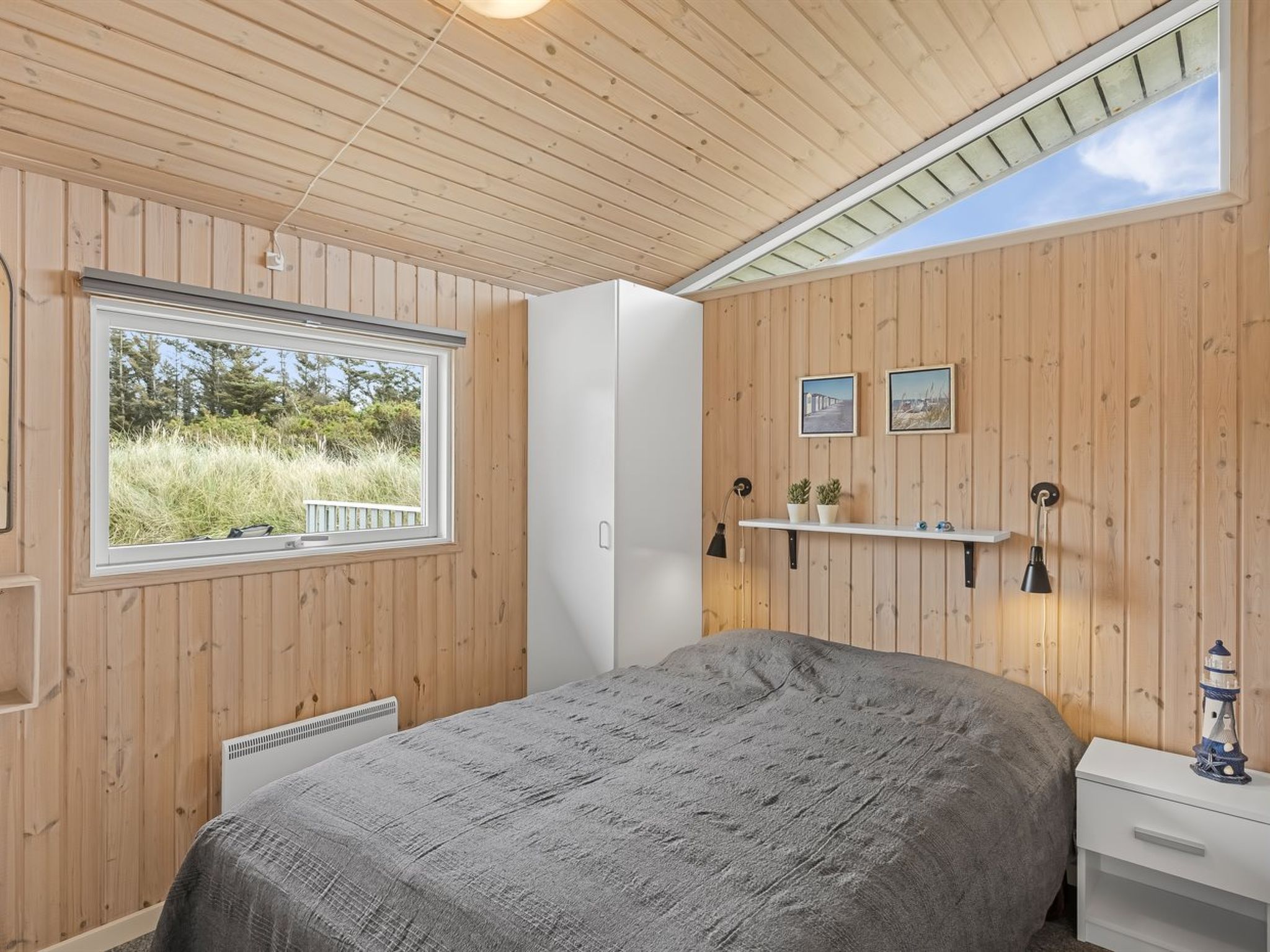 Een slaapkamer met een bed, een raam, een witte kledingkast en een plank met twee ingelijste foto's.