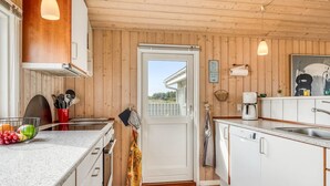 Una cocina con paredes de madera, armarios blancos, encimera de granito y vistas a través de una puerta.