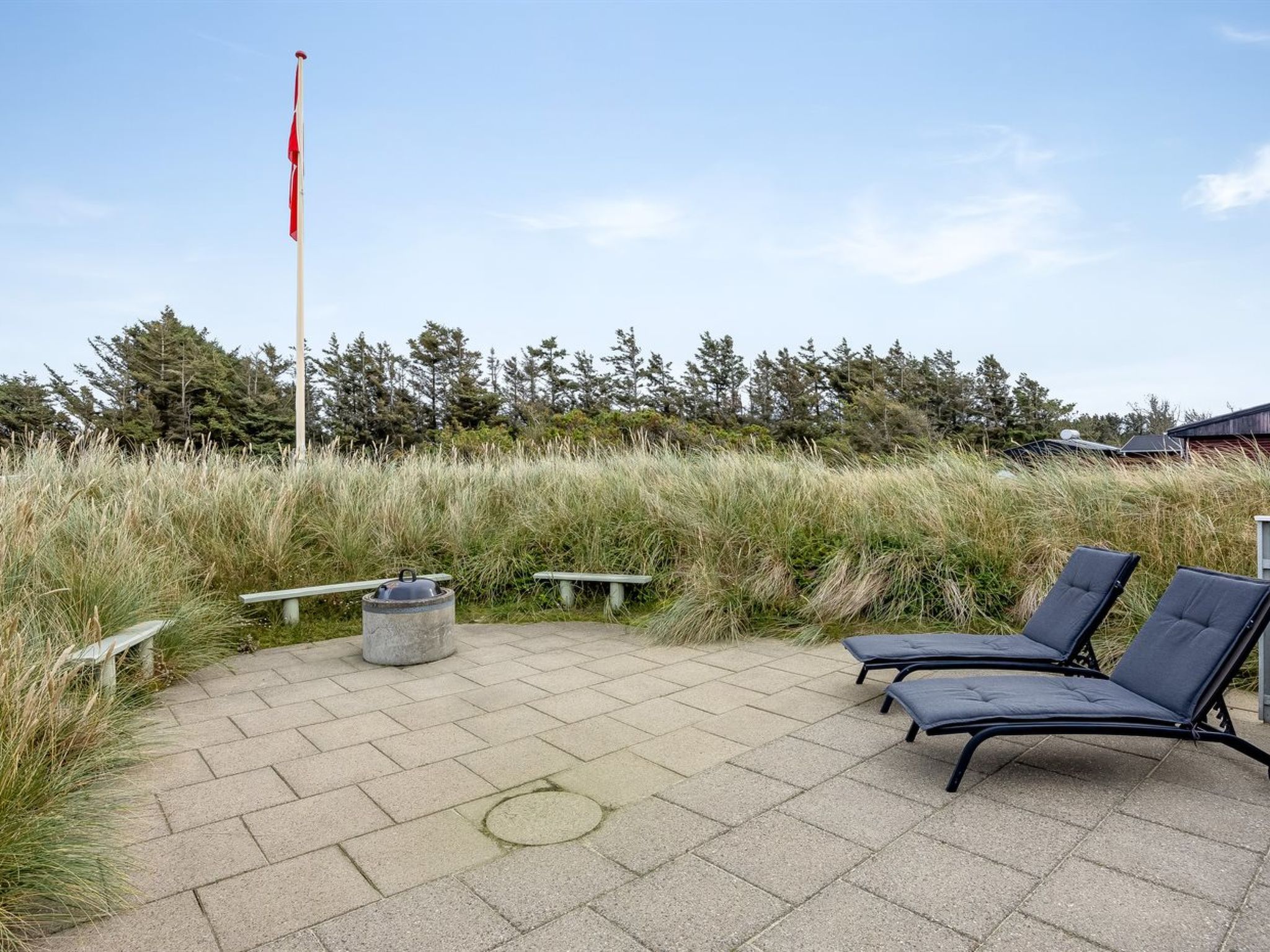 Een terras met lounge fauteuils en een bankje, omgeven door hoog gras en bomen.