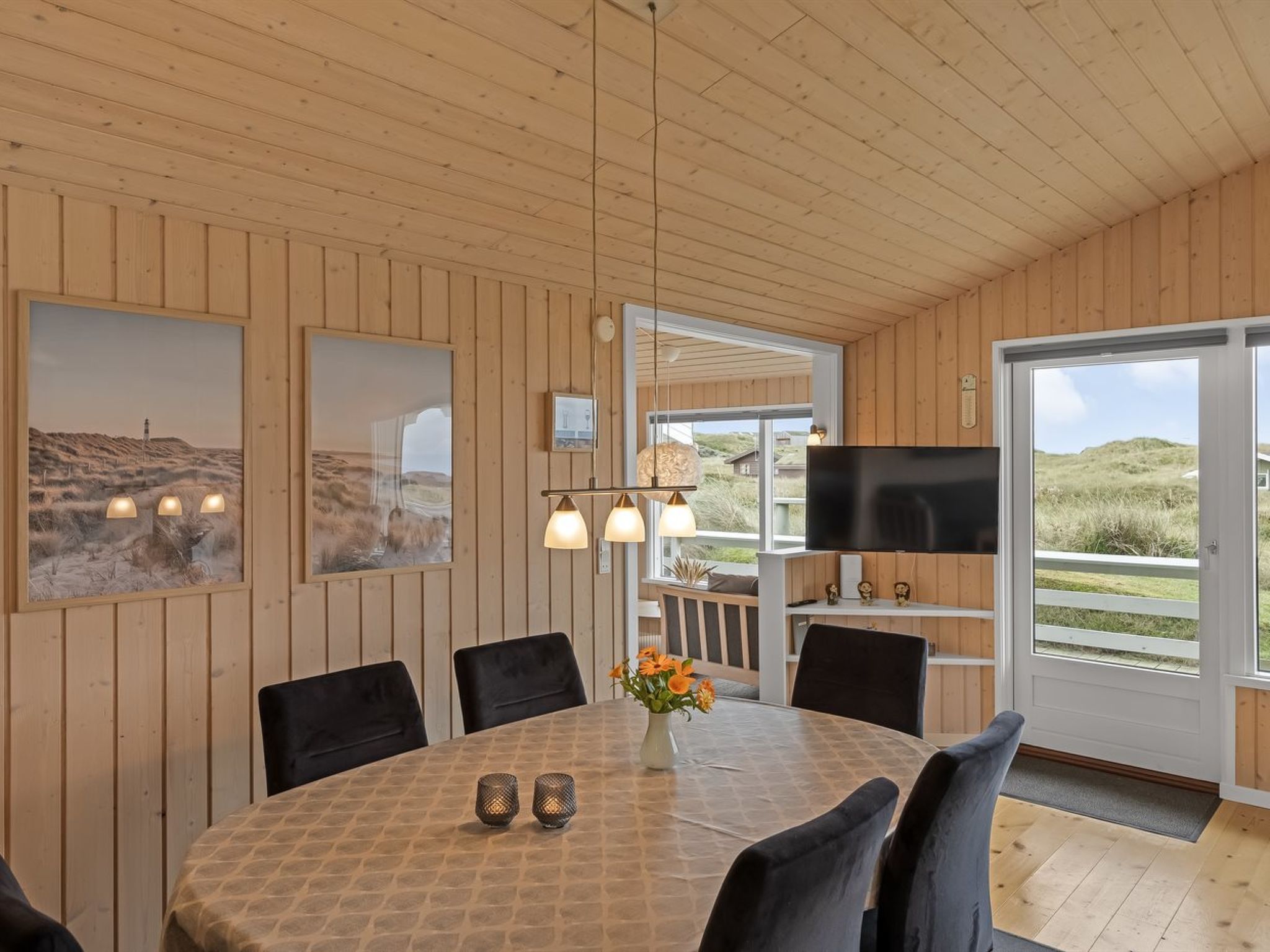 Een eethoek met een ronde tafel, stoelen, een vaas met bloemen en een televisie op een plank.