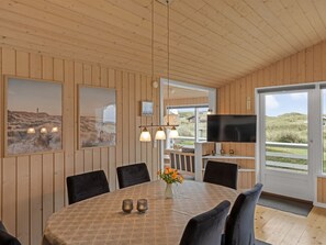 A dining area with a round table, chairs, a vase with flowers, and a television on a shelf. - "Fridgerd" - 300m from the sea by Interhome (Løkken)