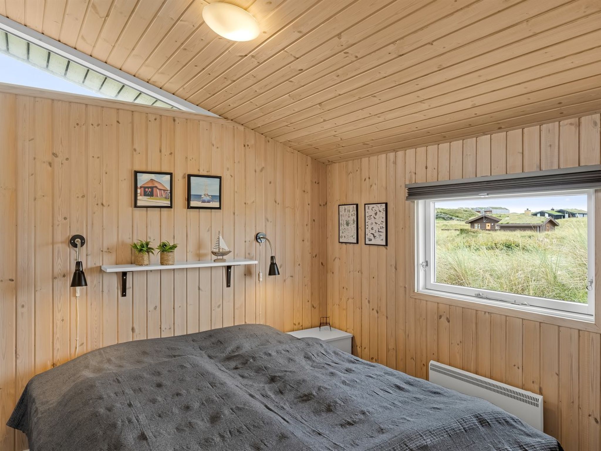 Een slaapkamer met een bed, houten wanden, een raam met uitzicht en wandplanken met decoratieve objecten.