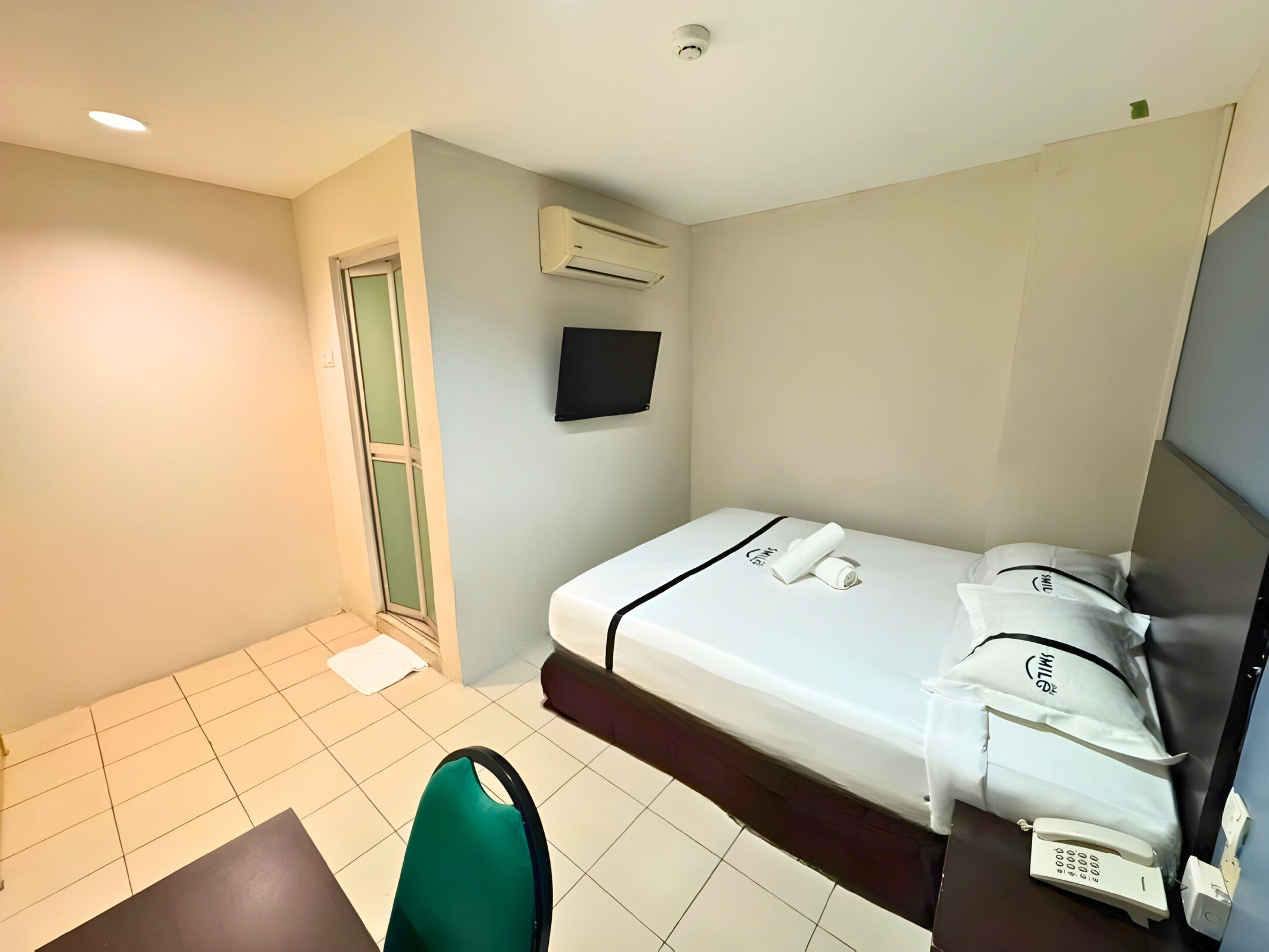 Habitación de hotel con cama, una silla, un escritorio, un televisor y un equipo de aire acondicionado.
