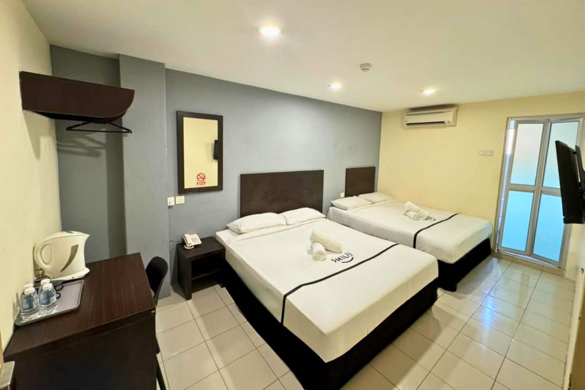 A hotel room with two beds, a desk with a telephone, a coffee maker, and a TV.