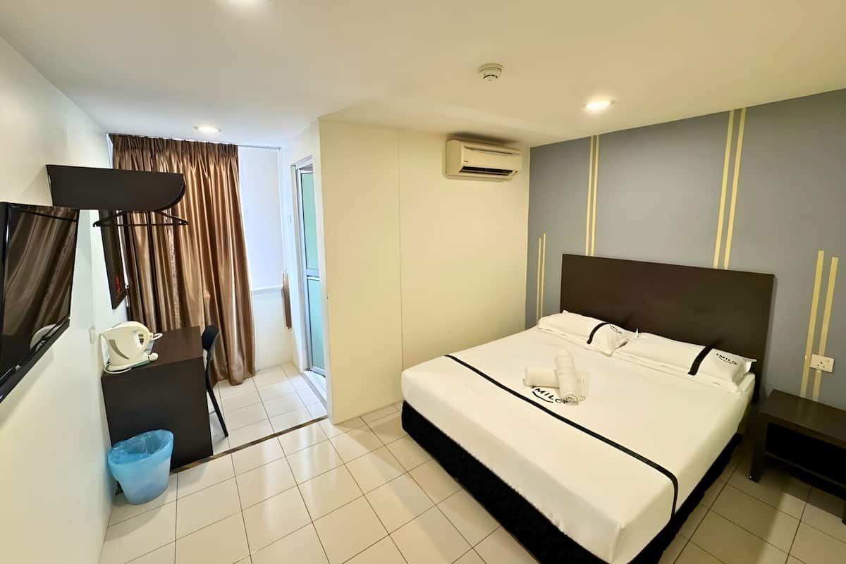 A hotel room with a bed, a desk, a chair, an air conditioning unit, and a television.