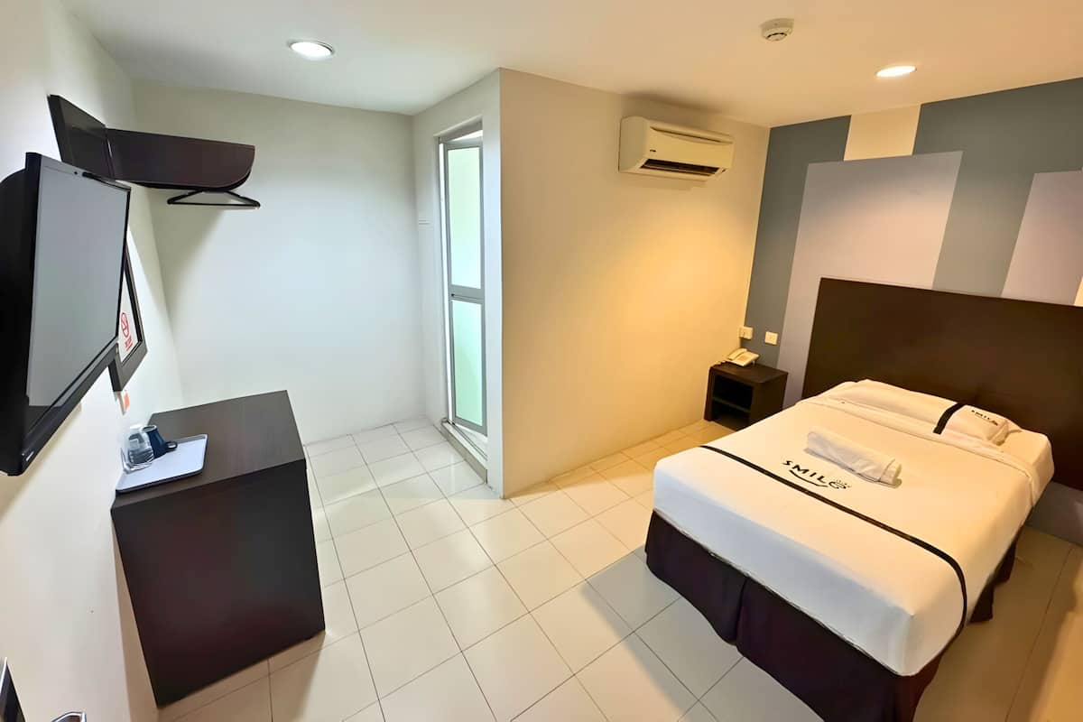 A hotel room with a bed, a desk, a TV, an air conditioning unit, and a window.