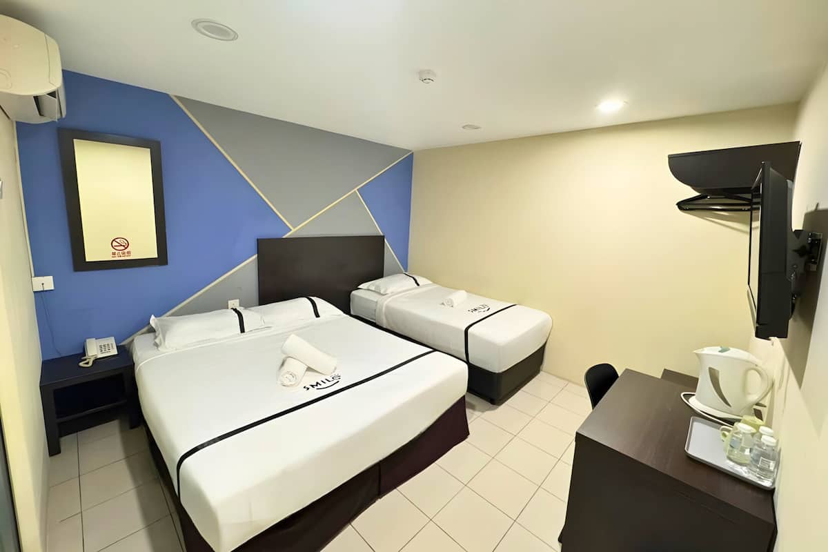 A hotel room with two beds, a desk with a coffee maker, a TV, and a wall-mounted mirror.