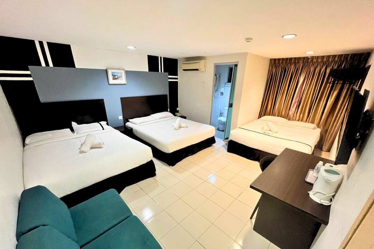 A hotel room with two beds, a sofa, a small table, and a bathroom visible through an open door.