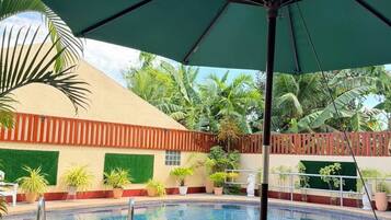 A swimming pool with lounge chairs, a green umbrella, and tropical plants.