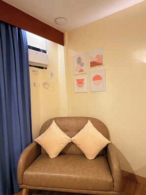 Una habitación con un sillón de cuero marrón, una cortina azul, un equipo de aire acondicionado y cuatro cuadros colgados en la pared.