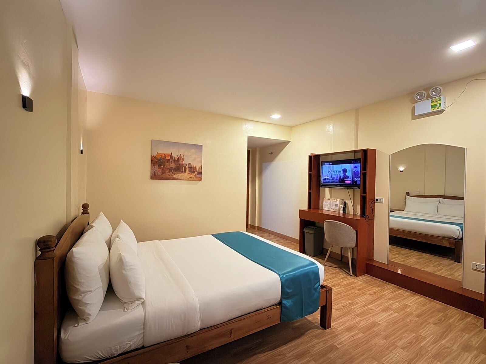 Een hotelkamer met een bed, een bureau met een computer, een televisie en een spiegel.