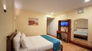 Een hotelkamer met een bed, een bureau met een computer, een televisie en een spiegel.