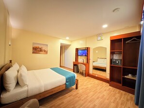 A hotel room with a bed, a desk with a chair, a television, a wardrobe, and a painting on the wall. - Rufana Suites (Moalboal)